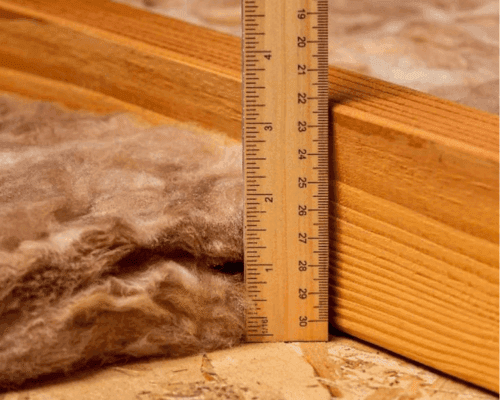 Ruler showing only a few inches of old fibreglass insulation against an attic joist